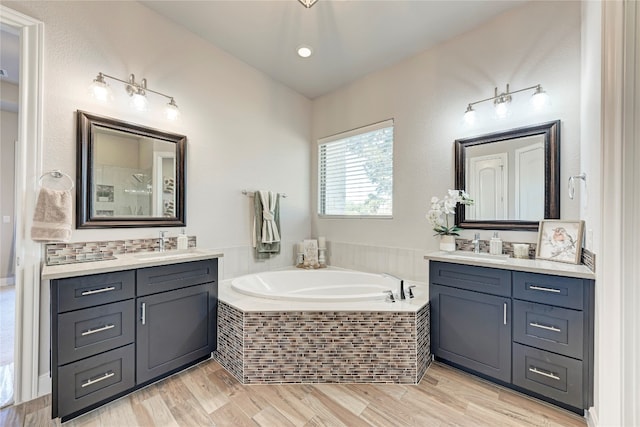 bathroom with vanity, tiled bath, and wood-type flooring