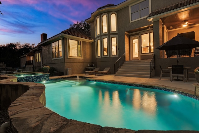 pool at dusk with an in ground hot tub and a patio