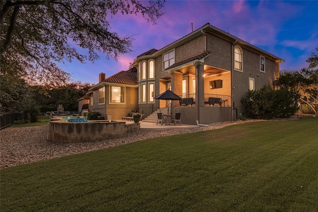 back house at dusk featuring a lawn and a patio area