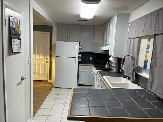 kitchen featuring decorative backsplash, white appliances, sink, light tile patterned flooring, and tile countertops