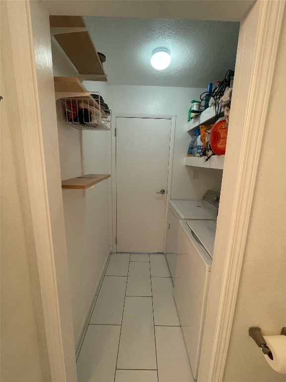 laundry room with light tile patterned flooring, washing machine and dryer, and a textured ceiling