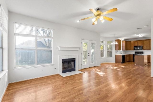 unfurnished living room featuring french doors, light wood-type flooring, ceiling fan with notable chandelier, sink, and a fireplace