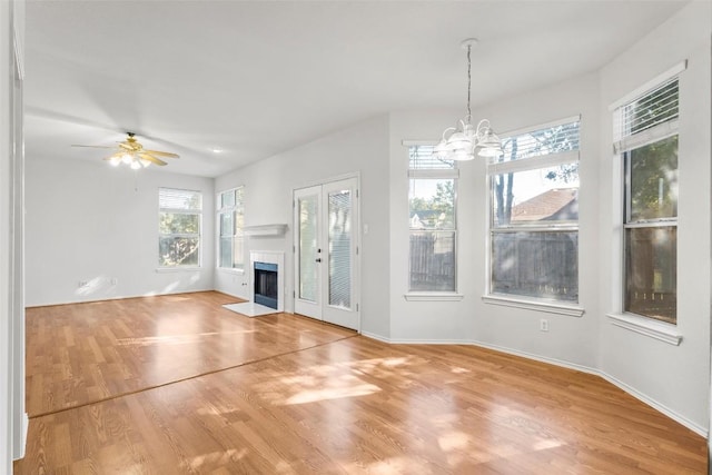 unfurnished living room featuring a healthy amount of sunlight, ceiling fan with notable chandelier, and wood-type flooring