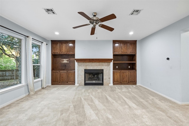 unfurnished living room with light carpet, a tile fireplace, ceiling fan, and a wealth of natural light