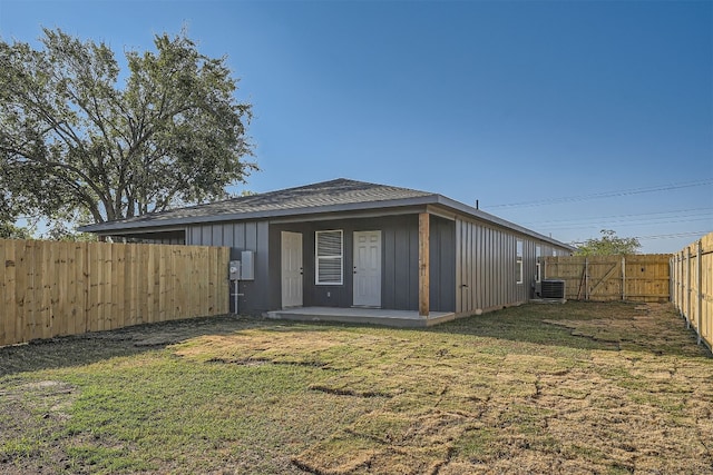 rear view of house with central air condition unit and a lawn