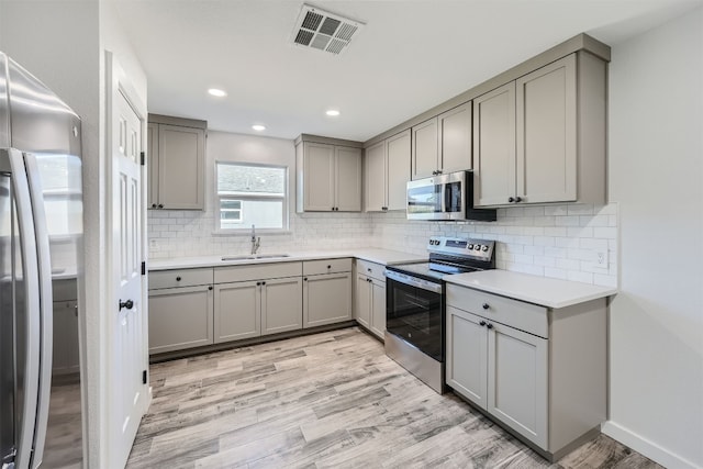 kitchen featuring light hardwood / wood-style floors, gray cabinets, tasteful backsplash, sink, and appliances with stainless steel finishes