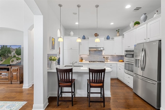 kitchen with dark hardwood / wood-style floors, pendant lighting, white cabinetry, appliances with stainless steel finishes, and a kitchen bar