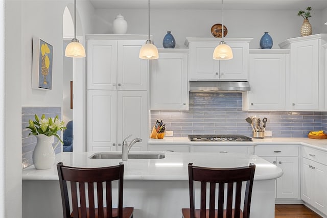 kitchen with white cabinets, hanging light fixtures, sink, stainless steel gas cooktop, and a kitchen bar