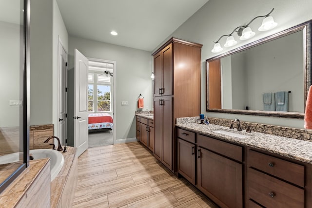 bathroom with vanity, ceiling fan, and tiled bath