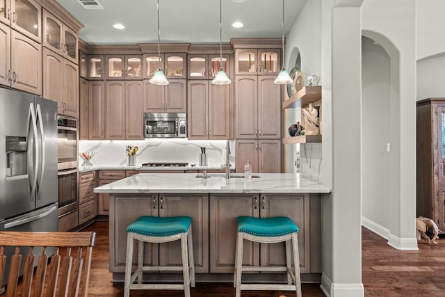 kitchen featuring kitchen peninsula, appliances with stainless steel finishes, light stone countertops, a breakfast bar, and sink