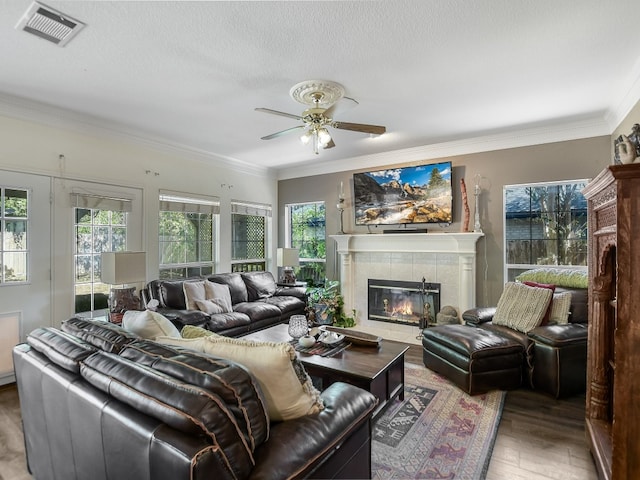 living room featuring ceiling fan, ornamental molding, wood-type flooring, a textured ceiling, and a fireplace