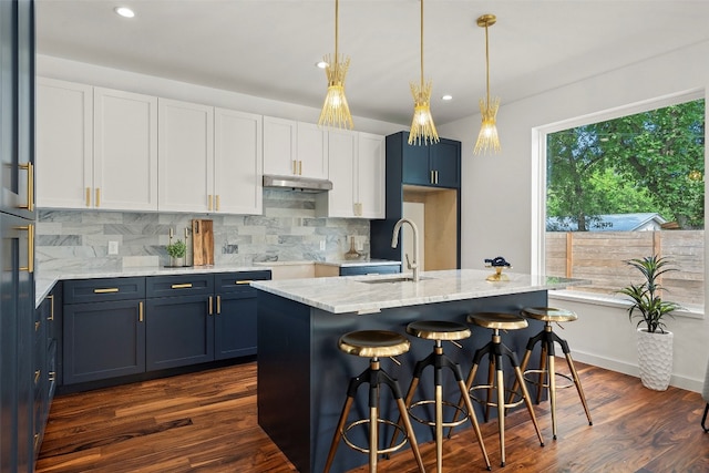 kitchen featuring dark wood-type flooring, hanging light fixtures, a center island with sink, and sink