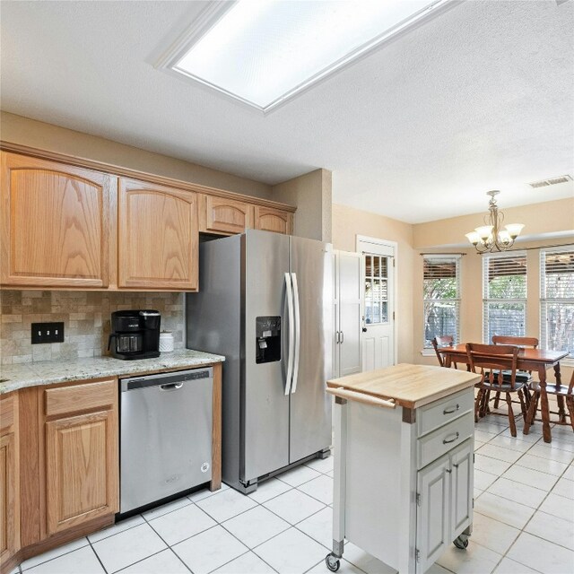 kitchen featuring tasteful backsplash, a kitchen island, a notable chandelier, stainless steel appliances, and light tile patterned floors