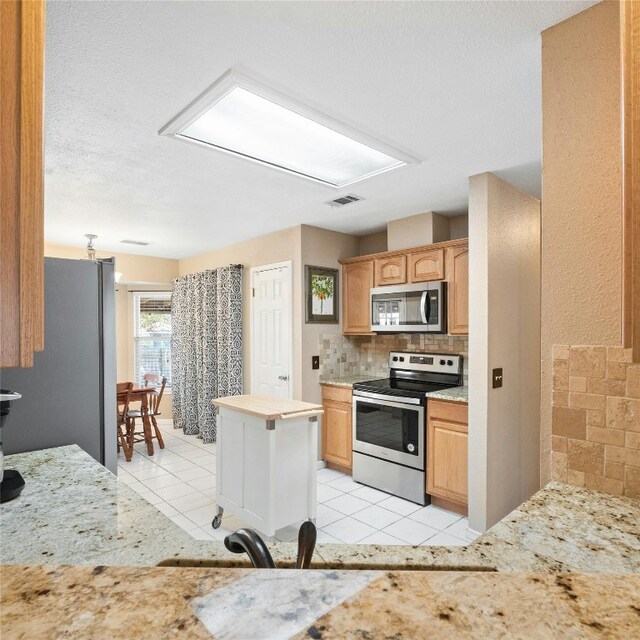 kitchen with a textured ceiling, stainless steel appliances, light tile patterned floors, and tasteful backsplash