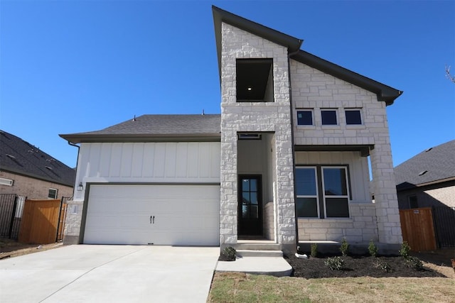 contemporary home with stone siding, fence, board and batten siding, concrete driveway, and a garage