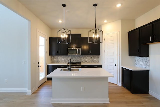 kitchen with stainless steel microwave, light countertops, an inviting chandelier, light wood-style floors, and a sink