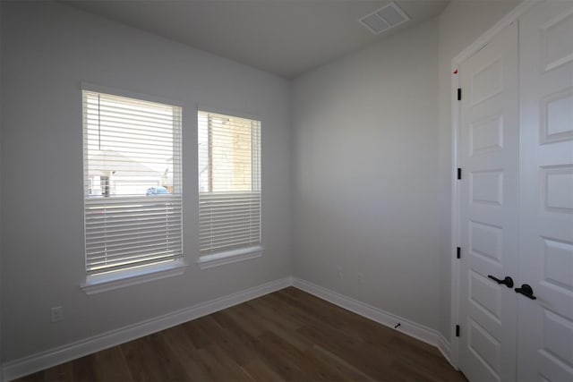 empty room featuring visible vents, baseboards, and dark wood-style flooring