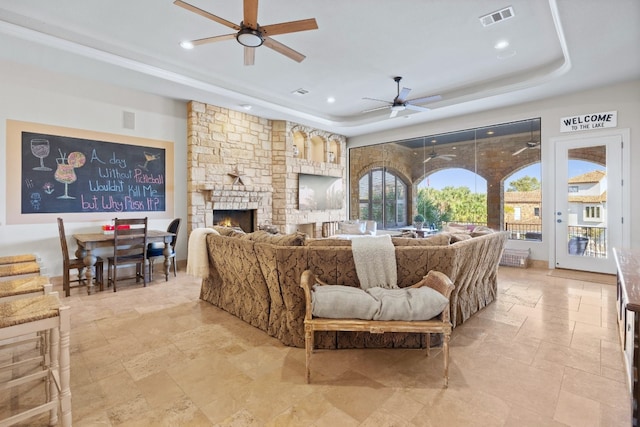 living room with a raised ceiling, ceiling fan, and a fireplace