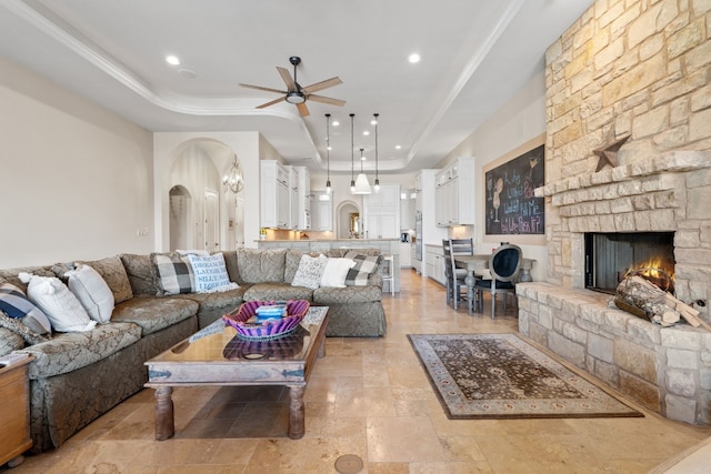 living room featuring a tray ceiling, a stone fireplace, and ceiling fan