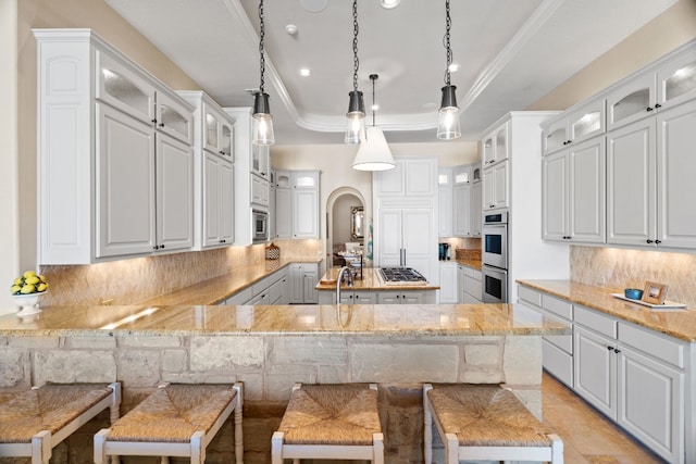 kitchen with a tray ceiling, backsplash, a breakfast bar, and hanging light fixtures