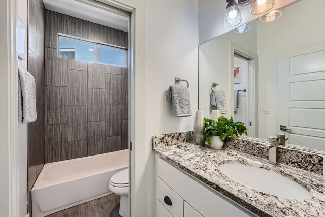 full bathroom featuring wood-type flooring, tiled shower / bath, vanity, and toilet