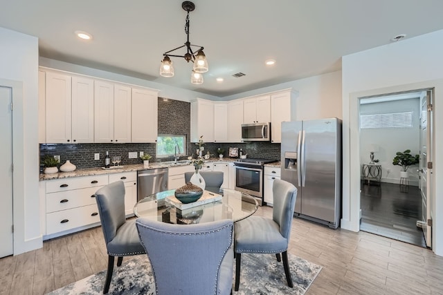 kitchen featuring tasteful backsplash, light hardwood / wood-style flooring, decorative light fixtures, appliances with stainless steel finishes, and white cabinetry