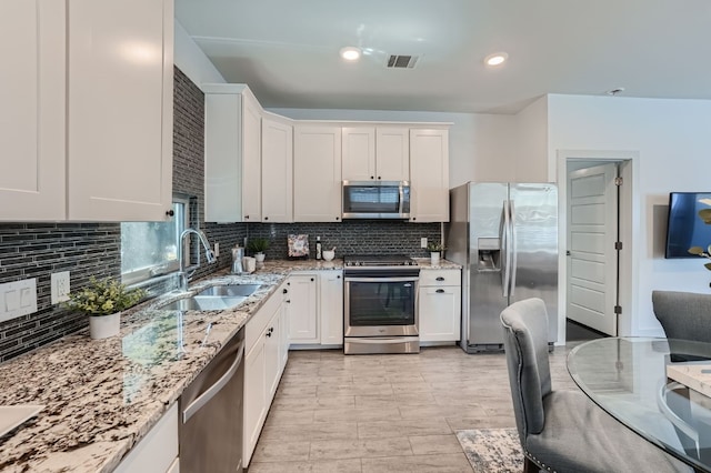 kitchen with sink, backsplash, white cabinetry, appliances with stainless steel finishes, and light stone countertops