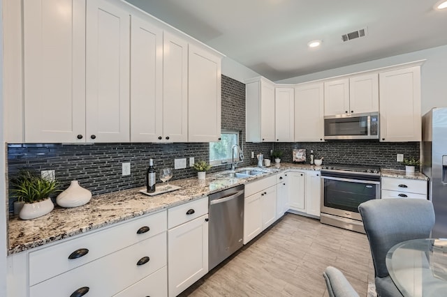 kitchen featuring light stone countertops, tasteful backsplash, sink, white cabinetry, and appliances with stainless steel finishes