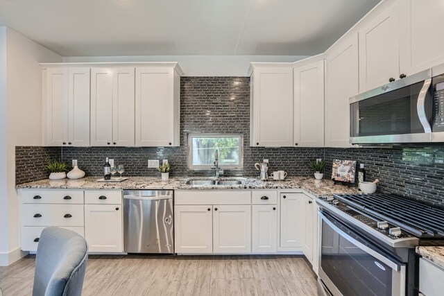 kitchen with stainless steel appliances, light wood-type flooring, sink, and white cabinetry