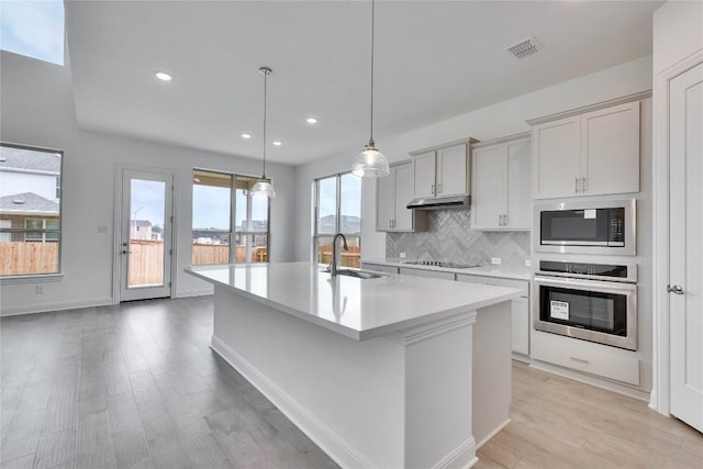 kitchen featuring decorative backsplash, built in microwave, under cabinet range hood, stainless steel oven, and a sink