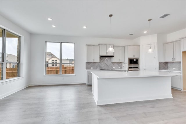 kitchen with pendant lighting, light countertops, visible vents, appliances with stainless steel finishes, and a kitchen island with sink