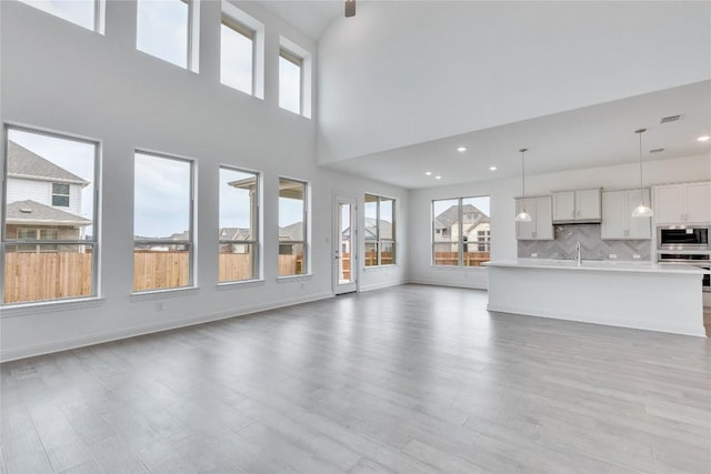 unfurnished living room with light wood-type flooring, plenty of natural light, baseboards, and a sink