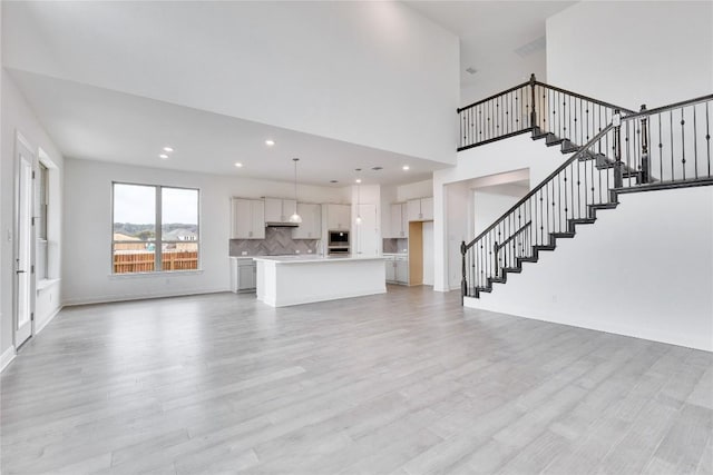 unfurnished living room featuring a towering ceiling, light wood-style floors, stairway, and recessed lighting