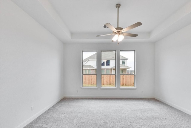 carpeted spare room with a raised ceiling, ceiling fan, and baseboards