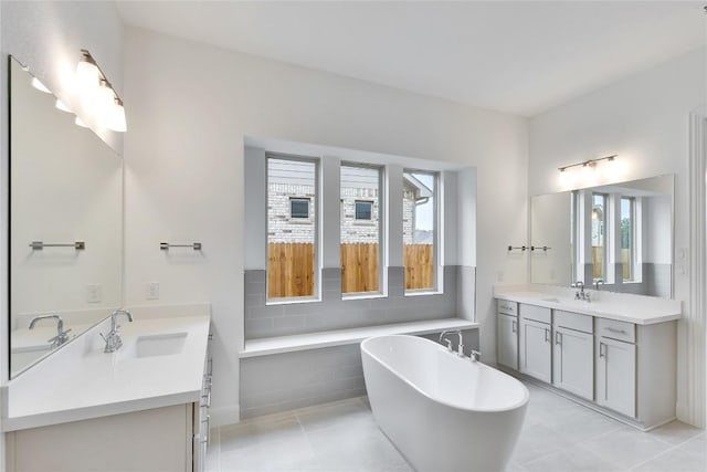 full bath with tile patterned flooring, a freestanding tub, two vanities, and a sink