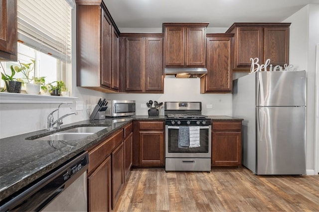 kitchen with stainless steel appliances, dark stone counters, hardwood / wood-style flooring, and sink