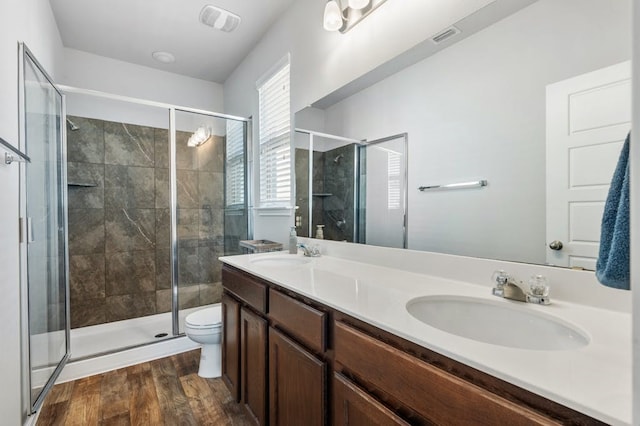 bathroom with wood-type flooring, a shower with shower door, vanity, and toilet