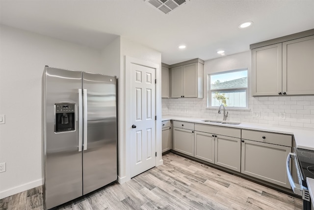 kitchen featuring light wood-type flooring, stainless steel appliances, tasteful backsplash, gray cabinetry, and sink