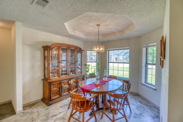 dining space with an inviting chandelier, a textured ceiling, and a tray ceiling