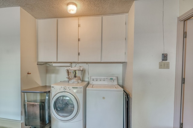 clothes washing area with washer and clothes dryer, a textured ceiling, and cabinets