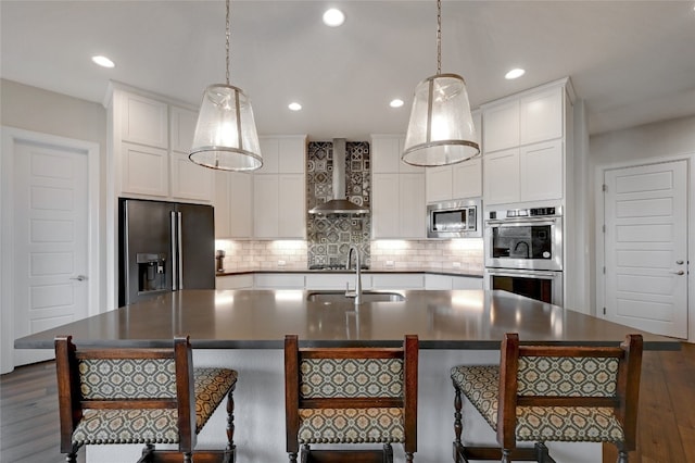 kitchen featuring an island with sink, appliances with stainless steel finishes, dark hardwood / wood-style floors, and wall chimney range hood