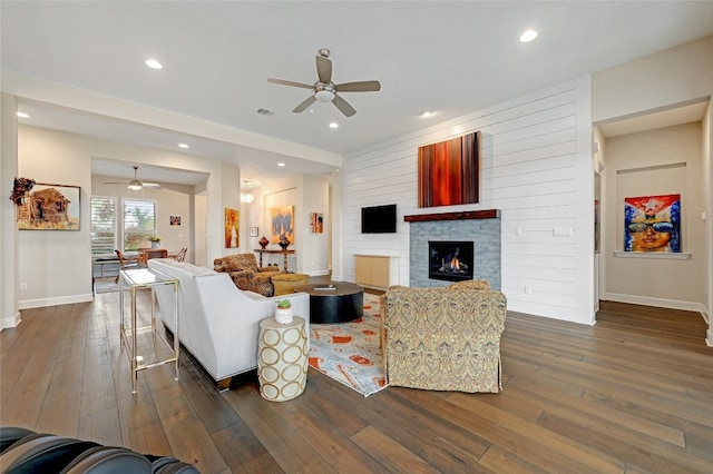 living room with ceiling fan, a stone fireplace, and dark hardwood / wood-style flooring