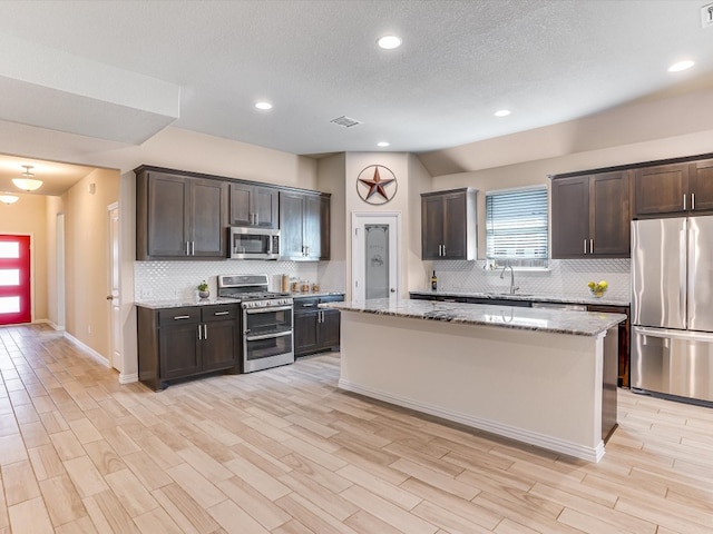 kitchen with light hardwood / wood-style floors, a kitchen island, dark brown cabinets, light stone counters, and stainless steel appliances