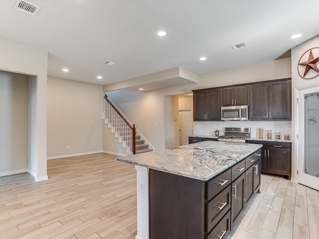 kitchen with light wood-type flooring, dark brown cabinetry, a center island, stainless steel appliances, and backsplash