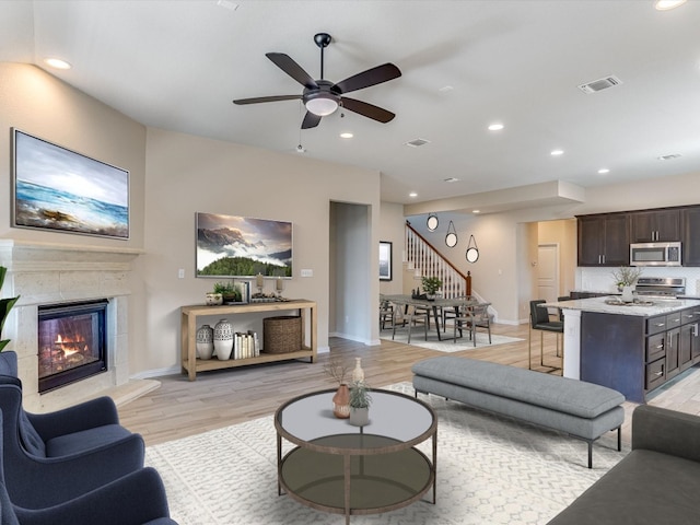 living room with ceiling fan, light wood-type flooring, and a fireplace