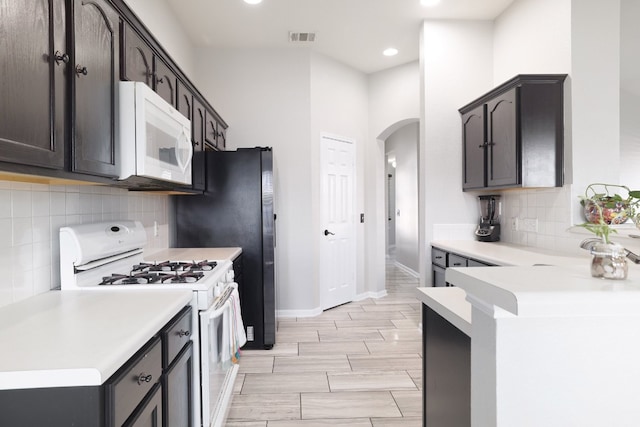 kitchen featuring dark brown cabinets, light wood-type flooring, tasteful backsplash, and white appliances