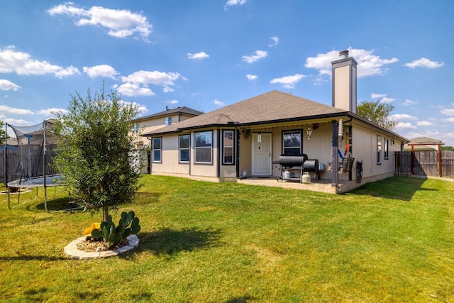 back of property with a trampoline, a lawn, and a patio