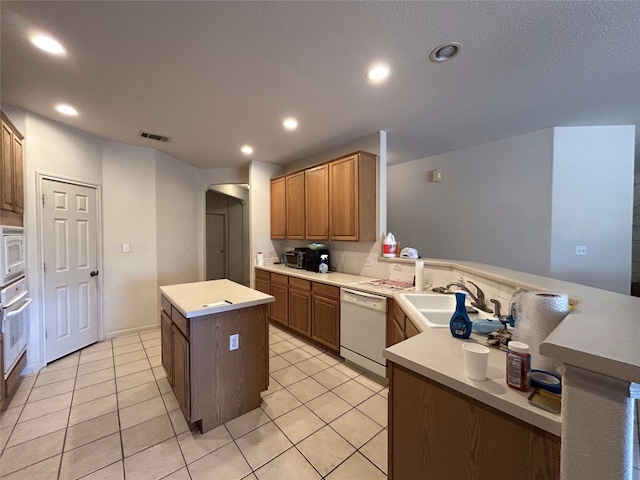 kitchen with light tile patterned flooring, sink, kitchen peninsula, appliances with stainless steel finishes, and a center island