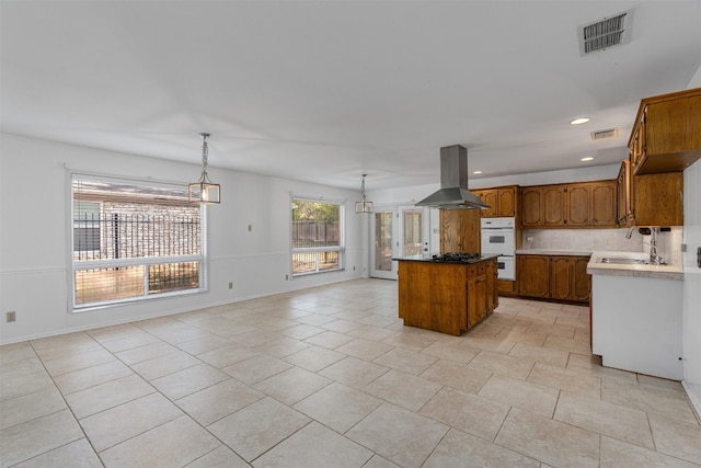 kitchen featuring tasteful backsplash, stainless steel gas cooktop, island exhaust hood, decorative light fixtures, and a center island