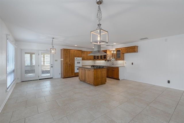 kitchen featuring hanging light fixtures, island range hood, double oven, a center island, and decorative backsplash